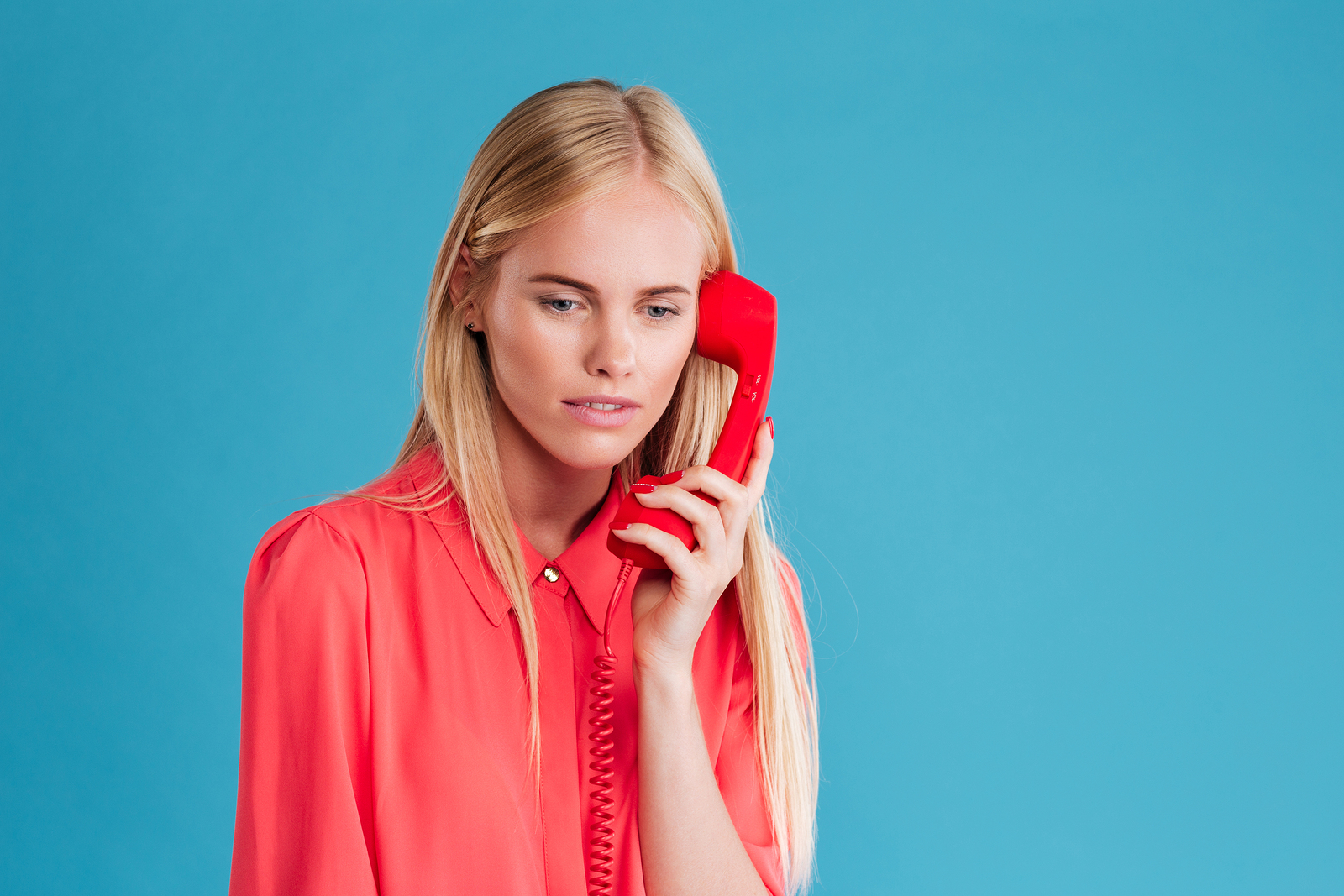 Sad blonde woman holding phone tube isolated on a blue background